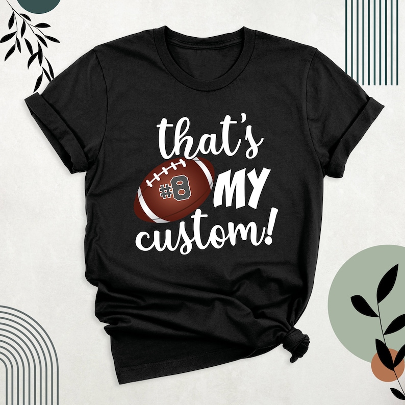 K&ouml;nnte beinhalten: Schwarzes T-Shirt mit wei&szlig;em Text, der "that's my custom!" lautet, und einem braunen und wei&szlig;en Fu&szlig;ball mit der Nummer 8 darauf.
