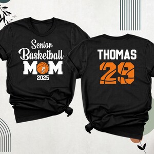 May include: Two black t-shirts. One shirt says "Senior Basketball Mom 2025" with a basketball graphic. The other shirt says "Thomas 29" with a basketball graphic.