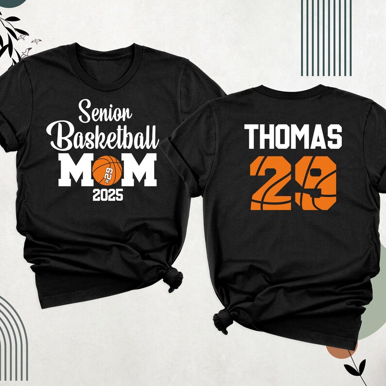 May include: Two black t-shirts. One shirt says "Senior Basketball Mom 2025" with a basketball graphic. The other shirt says "Thomas 29" with a basketball graphic.