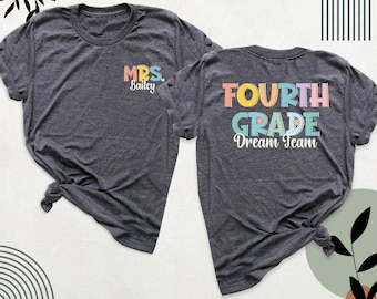 Puede incluir: Una camiseta de manga corta gris jaspeado oscuro mostrada de frente y de espaldas. El frente presenta el texto "MRS. Bailey" en letras coloridas. La parte posterior muestra el texto "FOURTH GRADE Dream Team" en letras grandes y multicolores.