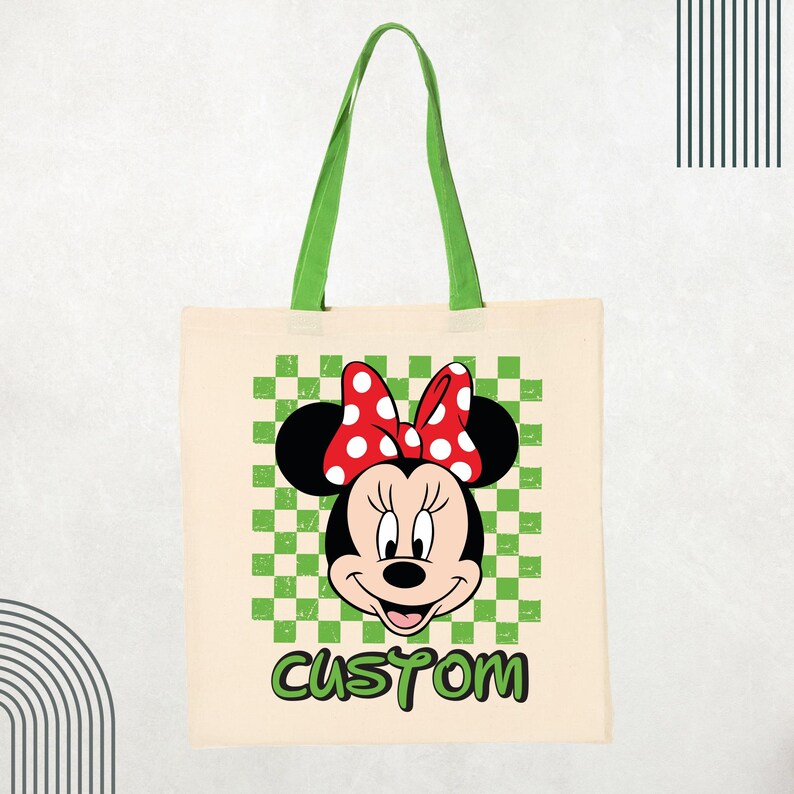May include: A beige canvas tote bag with green fabric handles. The front features a graphic of Minnie Mouse wearing a red and white polka dot bow, centered over a green and white checkered square. The word CUSTOM is printed in green below.