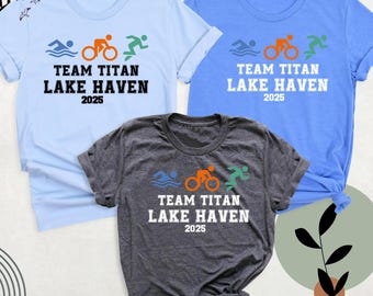 May include: Three short-sleeved t-shirts in light blue, blue, and charcoal gray. Each shirt features a triathlon graphic with the text "TEAM TITAN LAKE HAVEN 2025". The graphic includes a swimmer, cyclist, and runner.