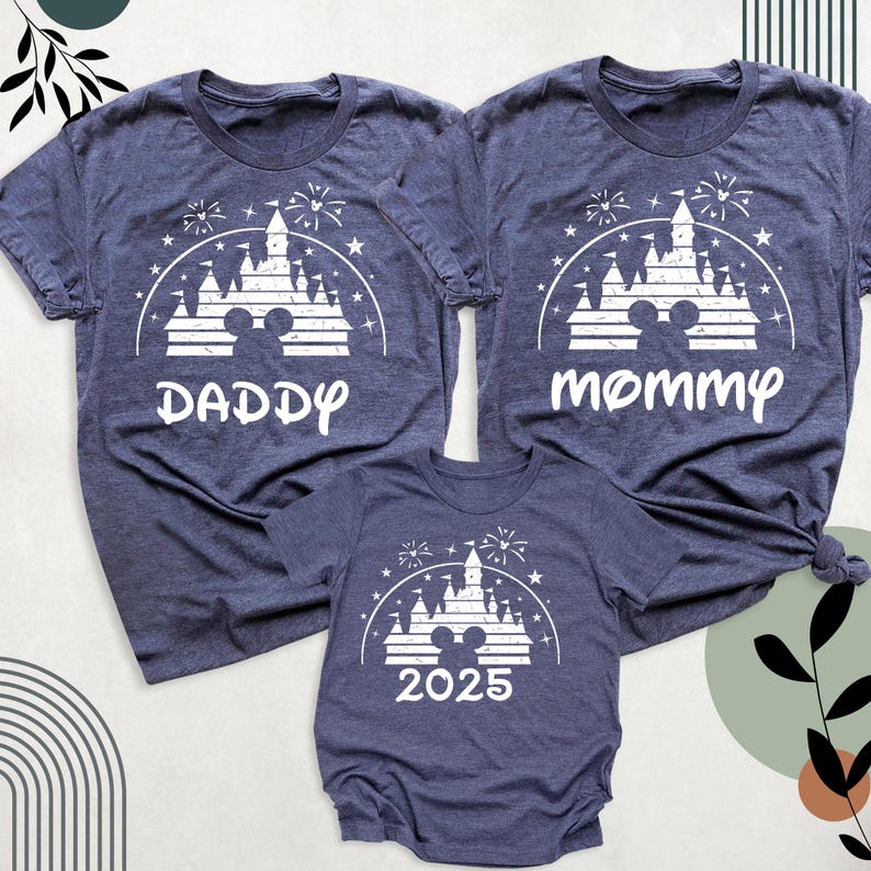 May include: Three navy blue t-shirts featuring a white castle, fireworks, and Mickey Mouse ears graphic. The shirts are labelled "Daddy", "Mommy", and "2025". The shirts are short-sleeved.