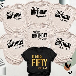 May include: Six beige t-shirts with black text that reads "fifty birthday" and either "crew" or "squad". One black t-shirt with gold text that reads "hello fifty est. 1974".