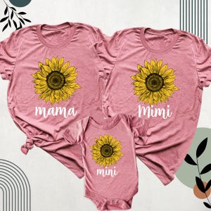 May include: Three matching pink t-shirts and a onesie. Each garment features a large yellow sunflower graphic with a brown center. The shirts are labeled "mama" and "Mimi", while the onesie says "mini".