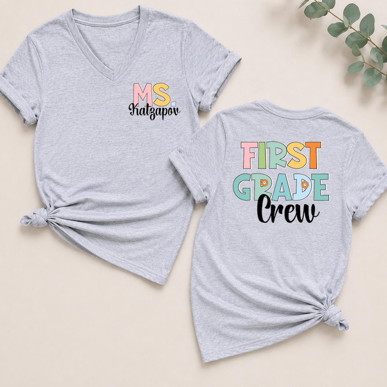 K&ouml;nnte beinhalten: Zwei graumelierte V-Ausschnitt-T-Shirts. Das linke T-Shirt zeigt den Text MS. Katzapov in Pink, Gelb und Schwarz. Das rechte T-Shirt zeigt den Text FIRST GRADE Crew in Pink, Orange, T&uuml;rkis und Schwarz mit kleinen orangefarbenen Blumen-Icons.