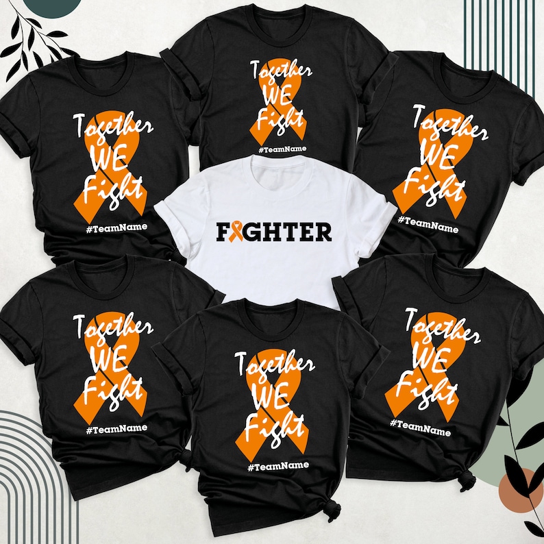 Op de afbeelding: Zes zwarte T-shirts met een oranje lintontwerp en de tekst "Together We Fight" en "#TeamName". Een wit T-shirt met een oranje lint en de tekst "FIGHTER".