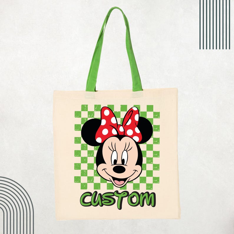 May include: A beige canvas tote bag with green fabric handles. The front features a graphic of Minnie Mouse wearing a red and white polka dot bow, centered over a green and white checkered square. The word CUSTOM is printed in green below.