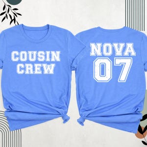 K&ouml;nnte beinhalten: Zwei hellblaue T-Shirts. Auf einem steht "COUSIN CREW" in wei&szlig;en Blockbuchstaben. Auf dem anderen steht "NOVA 07" in wei&szlig;en Blockbuchstaben. Beide Shirts sind unten geknotet.