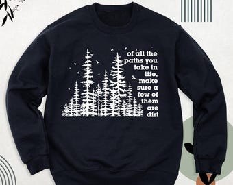May include: A dark navy blue crewneck sweatshirt featuring a white graphic of a pine forest and birds. The text reads: of all the paths you take in life, make sure a few of them are dirt. The garment has long sleeves and ribbed cuffs.