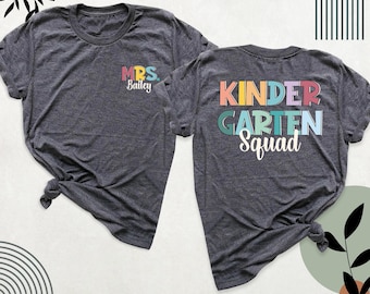 May include: A dark heather gray t-shirt shown from the front and back. The front features the text MRS. Bailey in colorful letters. The back displays the text KINDERGARTEN Squad in large, multi-colored block letters with a white script font.
