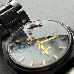 May include: Close-up of a vintage Orient watch with a dark blue face and gold-colored hands and markers. The watch has a stainless steel band and a clear crystal. The watch face has a textured pattern.