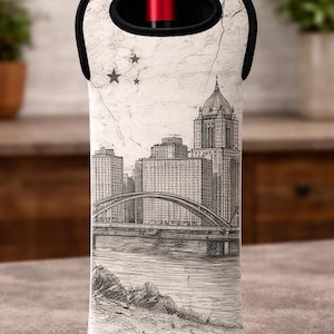 May include: A white wine bottle carrier with a black and white cityscape design. The illustration features a bridge, buildings, and stars. The carrier has a black handle and a red bottle top is visible.