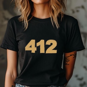 Peut inclure: Un t-shirt noir à manches courtes avec le nombre 412 imprimé en couleur or clair texturé sur la poitrine. Le vêtement présente une encolure ronde classique et un ourlet droit, offrant un aspect simple et épuré pour une tenue décontractée.
