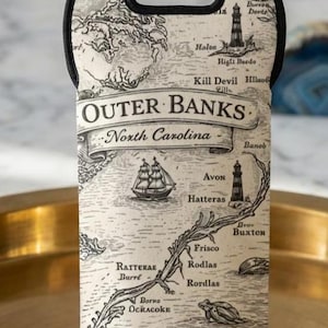 May include: A neoprene wine bottle carrier featuring a map of the Outer Banks, North Carolina. The black and white design includes nautical elements, place names, and the text "Outer Banks". It has a black handle.