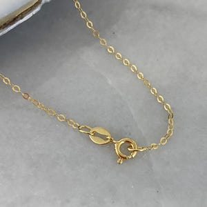 May include: A delicate gold chain necklace featuring thin, interlocking oval links and a secure spring ring clasp. The metal has a polished, reflective finish, and the chain is shown in its entirety with the clasp mechanism clearly visible.
