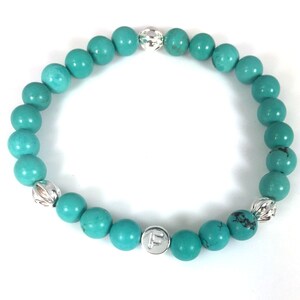 May include: Turquoise beaded bracelet with silver accents and a silver charm with the letter "F" on it.