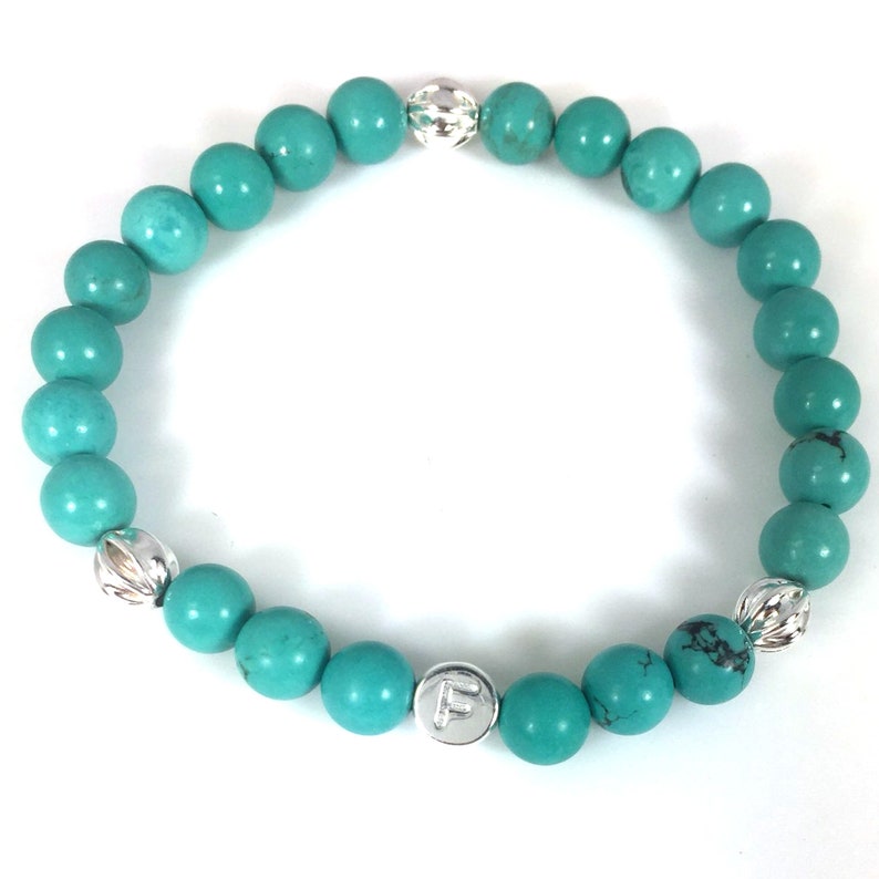 May include: Turquoise beaded bracelet with silver accents and a silver charm with the letter "F" on it.