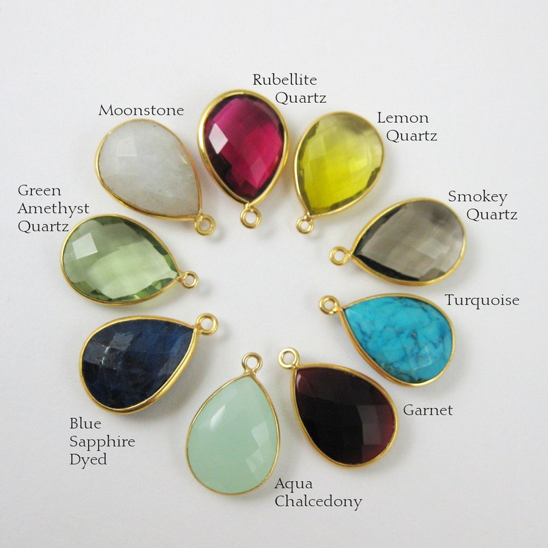May include: Assortment of 10 teardrop-shaped gemstone pendants with gold-toned settings. The stones include moonstone, rubellite quartz, lemon quartz, green amethyst quartz, blue sapphire, aqua chalcedony, smokey quartz, turquoise, and garnet.