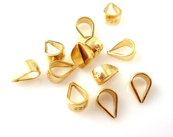 May include: A group of ten gold-colored metal pendant bails, each with a teardrop shape and a small loop at the top. The bails are scattered on a white surface.
