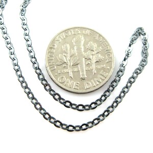 May include: A black chain necklace with a curb link style. The chain is shown next to a US dime for size comparison.