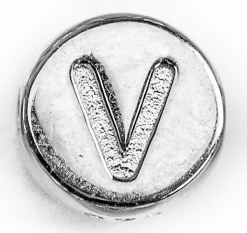 May include: A silver-coloured metal charm with the letter V embossed on it.