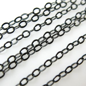 May include: Black chain links in a variety of sizes, arranged in rows on a white surface. The chain links are all oval shaped and have a smooth, polished finish.