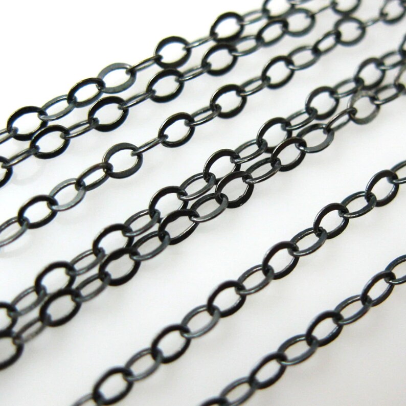 May include: Black chain links in a variety of sizes, arranged in rows on a white surface. The chain links are all oval shaped and have a smooth, polished finish.