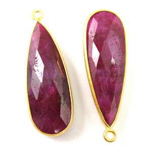 May include: Two teardrop-shaped ruby red gemstone pendants with gold-toned metal settings and jump rings.