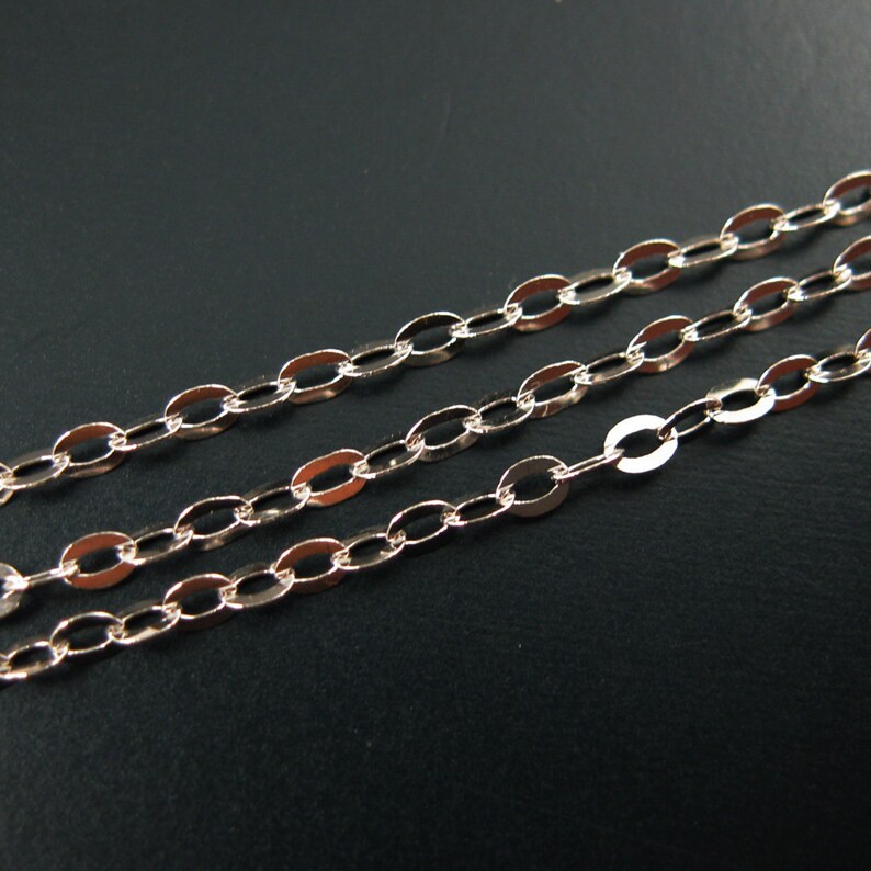 May include: Three strands of gold-toned oval link chain, lying flat on a black surface.