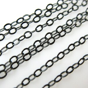 May include: Multiple strands of black chain, each with oval links, are laid out in parallel lines on a white surface.