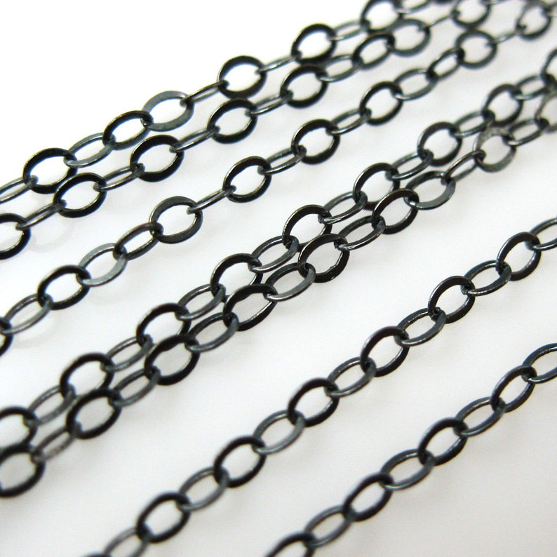 May include: Multiple strands of black chain, each with oval links, are laid out in parallel lines on a white surface.