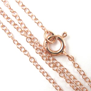 May include: A rose gold chain necklace with a lobster clasp closure. The chain is made of small, oval-shaped links.