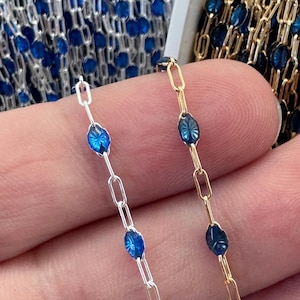 May include: Close-up of two chains, one silver and one gold, each with oval blue gemstone accents. The silver chain is on the left, and the gold chain is on the right. The gemstones have a starburst design.