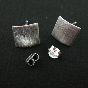 May include: A pair of silver square earrings with a brushed finish. The earrings have a post and butterfly backing.