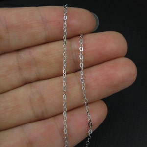 May include: A silver chain necklace with a delicate, thin design. The chain is shown on a hand, with the ends of the chain hanging down.