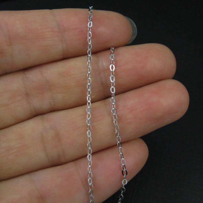 May include: A silver chain necklace with a delicate, thin design. The chain is shown on a hand, with the ends of the chain hanging down.