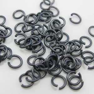 Op de afbeelding: Een stapel kleine, zilverkleurige springringen. De ringen zijn allemaal even groot en zijn in een willekeurig patroon gerangschikt.