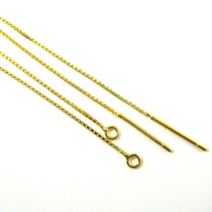 May include: Close-up of several gold-colored chain earrings. The earrings have a delicate, linear design with a small loop at the end of the chain. The chains are thin and rectangular, and the background is white.