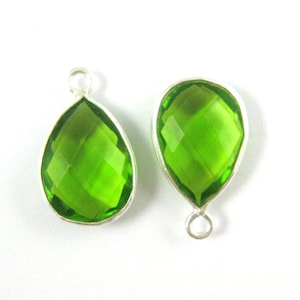 May include: Two green pear-shaped gemstone pendants with silver settings and jump rings. The gemstones are faceted and have a clear, bright green color.