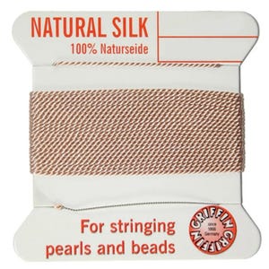 Op de afbeelding: Een spoel met natuurlijke zijden draad voor het rijgen van parels en kralen. De spoel is gelabeld met "NATURAL SILK 100% Naturseide" en "Voor het rijgen van parels en kralen".