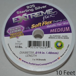 Op de afbeelding: Een spoel 925 Sterling Silver Extreme Flex Metallic Flex Wire, medium, met een diameter van 0,48 mm en een sterkte van 6,8 kg. De spoel is wit met paarse en witte tekst. De tekst luidt "Now with Extreme Abrasion Resistance".