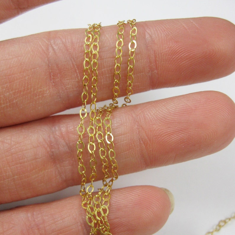 May include: A close-up of a gold chain, shown wrapped around a finger. The chain is made of small, oval-shaped links.