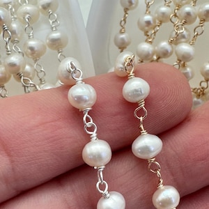 Puede incluir: Primer plano de un delicado collar de perlas. El collar presenta peque&ntilde;as perlas blancas redondas ensartadas con alambre de plata y oro. Las perlas tienen un brillo lustroso, y el alambre est&aacute; intrincadamente envuelto alrededor de cada perla, creando un aspecto refinado y elegante.