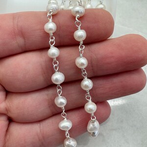 Puede incluir: Primer plano de dos hilos de pendientes de perlas blancas. Cada pendiente presenta m&uacute;ltiples perlas redondas ensartadas con alambre de plata. Las perlas tienen un brillo lustroso, y el alambre de plata a&ntilde;ade un delicado contraste.