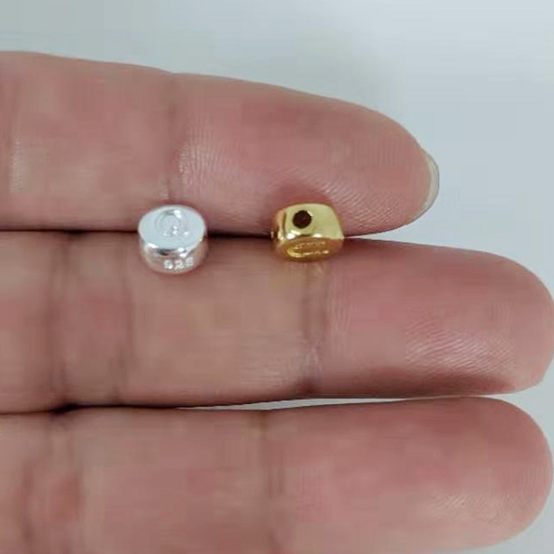 May include: Two small round beads, one silver and one gold, with a hole through the centre. The beads are approximately 5mm in diameter.