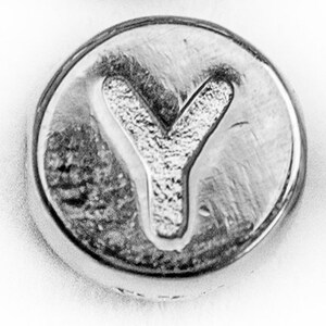 May include: A silver charm featuring the letter Y embossed on it.