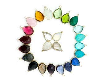 May include: A collection of 18 teardrop-shaped gemstone pendants with gold-toned jump rings. The gemstones are arranged in a circle with a cluster of four clear gemstones in the center. The gemstones include amethyst, aquamarine, citrine, emerald, garnet, green amethyst, labradorite, moonstone, peridot, rose quartz, ruby, sapphire, smoky quartz, topaz, turquoise, and white topaz.