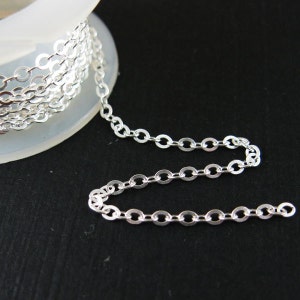 May include: A silver chain with round links, wound around a spool. The chain is laying on a black surface.