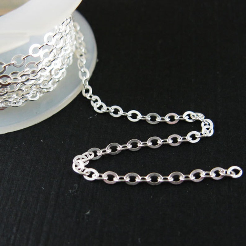 May include: A silver chain with round links, wound around a spool. The chain is laying on a black surface.
